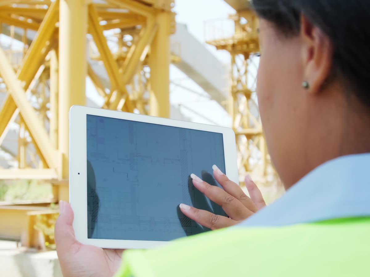 Cheffe de chantier consultant un plan sur sa tablette, devant une grue